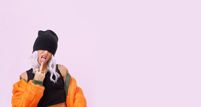 Blonde model in fashion urban street look. Trendy orange bomber jacket and stylish beanie cap. Middle finger provocation. Fall winter seasons lookbook