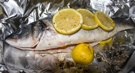 Fresh sea bass with lemon and spices on aluminum foil.