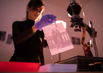Female photographer developing film and printing photographs in traditional process in darkroom....