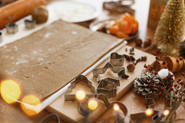 Raw gingerbread dough, metal cutters, spices, festive decorations and lights on rustic table