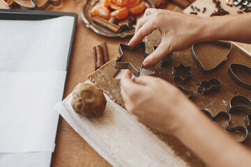Hands cutting gingerbread dough with star metal cutter on rustic table with festive decor