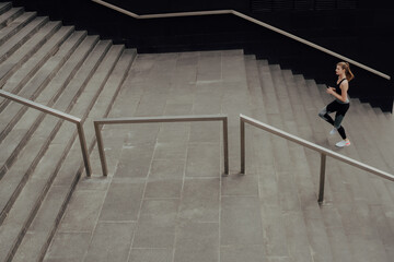 A young girl in a tracksuit runs up the stairs, in a business center.