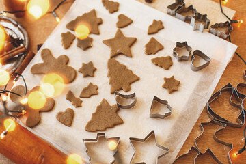 Raw gingerbread cookies in christmas shapes, metal cutters, decorations and lights on rustic table
