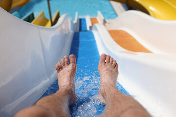 Male feet with splashing water on slide in water park. Entertainment in hotel pools and aquapark...