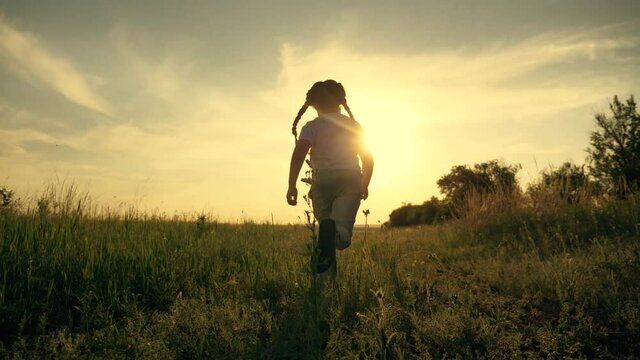 Girl is run along road. Childdream concept. Happy little girl at sunset. Kid run across field. Happy kid in field at sunset. Girl run along road at sunset. Happy family concept. Dream of child.