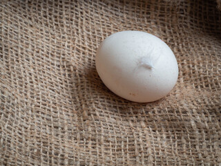 A white chicken egg lying on a burlap sack