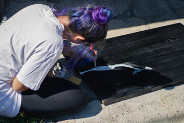 Latin hispanic woman with colorful hair painting a wooden board with black and white paint. Outdoors painting hobbie