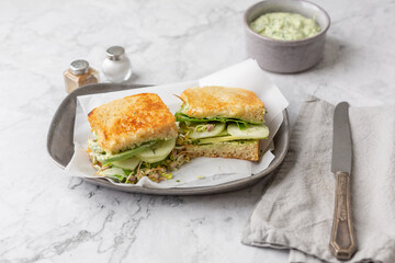 Green Goddess Sandwich on a Pewter Tray on a white Marble Countertop; Bowl of Green Goddess Dressing, Salt and Pepper, Knife, and Gray Napkin in Background
