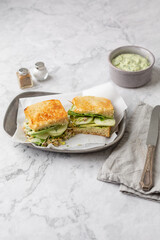 Green Goddess Sandwich on a Pewter Tray on a white Marble Countertop; Bowl of Green Goddess Dressing, Salt and Pepper, Knife, and Gray Napkin in Background
