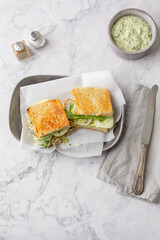 Green Goddess Sandwich on a Pewter Tray on a white Marble Countertop; Bowl of Green Goddess Dressing, Salt and Pepper, Knife, and Gray Napkin in Background