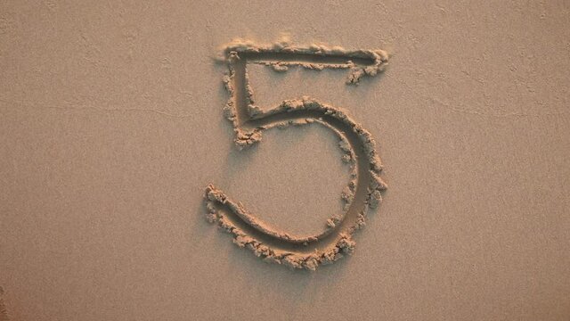 Number five written in the sand and washed by a wave