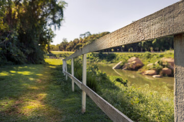 Fototapeta premium Paisagem em parque, com árvores, lago, sol forte e calor. Foco seletivo destaca a cerca.