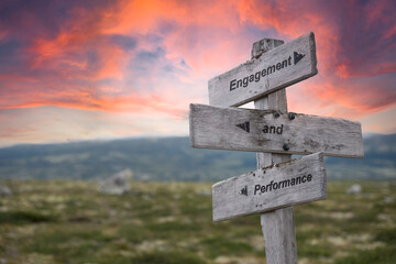 engagement and performance text engraved in wooden signpost outdoors in nature during sunset and pink skies.