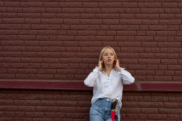 portrait of a young blonde girl of generation Y, in jeans and a white shirt, against a background of a red brick wall
