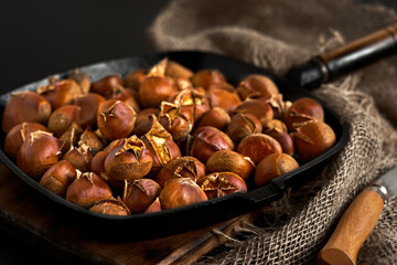 Close-up of delicious fried cracked chestnuts in a frying pan on a black background with burlap, Close-up. Chestnut for christmas or holidays, seasonal dish
