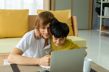 Young caucasian businessman and father working from home with notebook computer and taking care of little son in living room. Social distancing new normal concept.