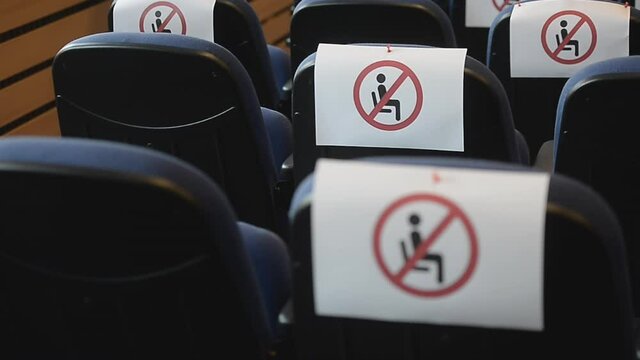 Shallow depth of field with social distance warning signs on seats during a show, concert or play in a theater or cinema, conference hall. Empty rows of places marked with a warning "'don't sit' sign.