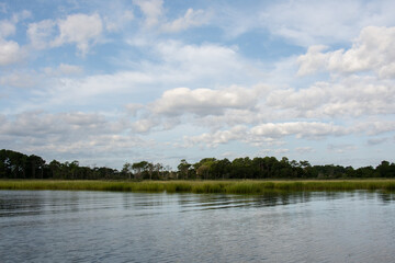 Blue sky and puffy white clouds above expansive bay water and natural shoreline