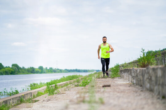 Athletic running guy in stylish sportswear on workout outside in cloudy weather, sport healthy lifestyle in urban