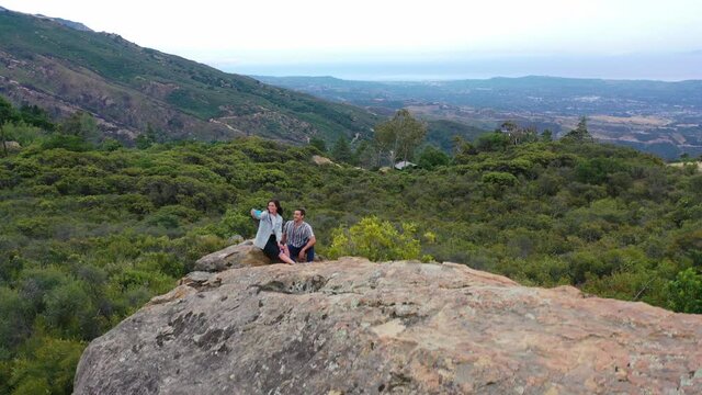 A man and woman climb a rock and take selfie photos overlooking Santa Barbara, California.