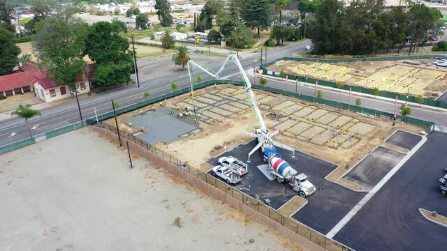 Remarkable aerial over construction site with giant crane and workers pouring concrete foundation in Ventura, California.