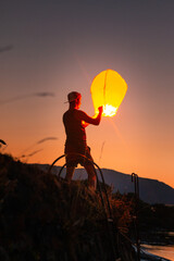 Teenager flying a chinese lantern at sunset time.
