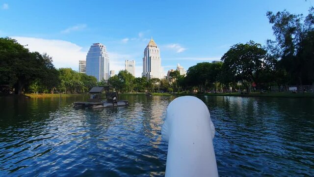 POV footage: Heads of a Swan paddle boat on the lake with Skyscrapers on the background in Lumphini Park, Bangkok, Thailand. Wide shot.