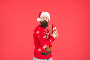Fototapeta na wymiar greedy bearded guy wearing funny knitted sweater and santa claus hat and hold present box has an idea for celebrating new year party, new year boxing day