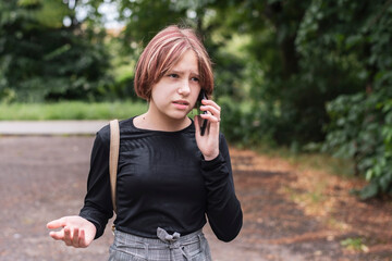 Fototapeta premium The young girl is talking on the phone with father, she is a little angry because she is clarifying the relationship with him, the girl has begun adolescence