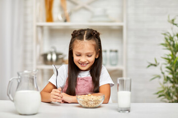 smiling cute little girl eating breakfast: cereal with the milk in the kitchen. healthy breakfast