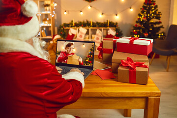 Santa looking at laptop screen spying on little boy who's writing and sending Christmas letter