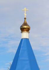 Orthodox Christian church with blue roof, golden dome and cross in Russia. A building for religious ceremonies with a bell tower against a cloudy sky