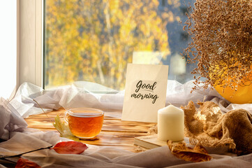 Cup on the window with sun and book. Yellow trees on the background. Autumn concept.