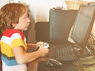 Little kid playing with joystick gamepad in front of PC at emulated video game.