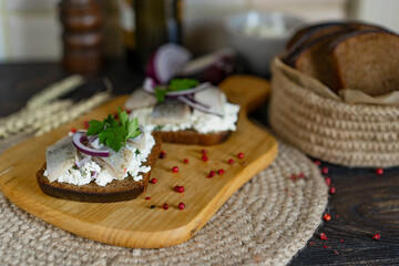 Brown whole grain bread with cottage cheese and salted herring, onion on a wooden cutting board, kitchen, natural day light.