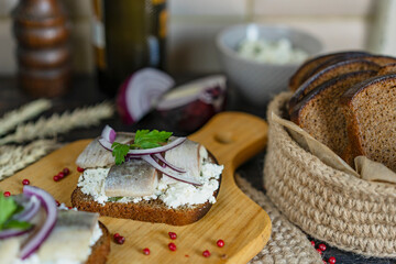 Brown whole grain bread with cottage cheese and salted herring, onion on a wooden cutting board, kitchen, natural day light.