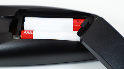Black TV remote control with AAA alkaline batteries in red and white on a white background. Battery...