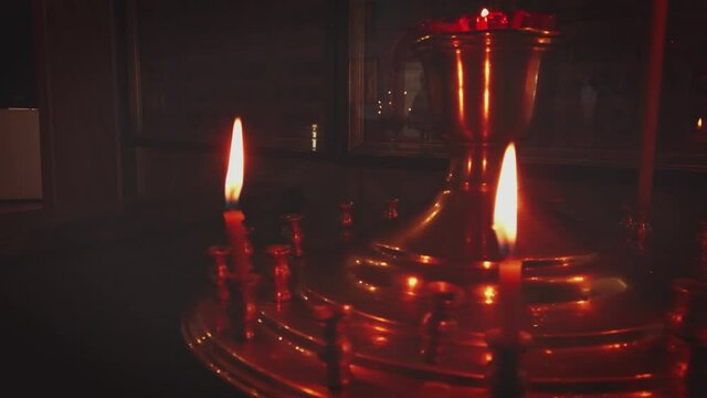 Golden candle stand in front of the orthodox icons (paintings of the saints) with some burning candles panning shot.