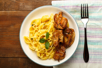 A light plate of pasta in a creamy sauce with cheese and chicken on the table on a napkin next to a fork.