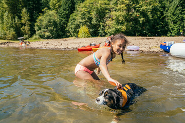 Happy girl swimming in lake with pet dog in life jacket