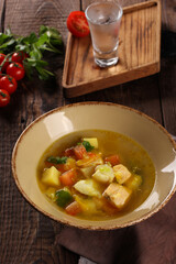 Oriental cuisine. Fish shurpa. Salmon and cod soup with potatoes, celery, sweet peppers, tomatoes in a beige bowl with on a wooden table. Glass of vodka. Rustic. Background image, copy space
