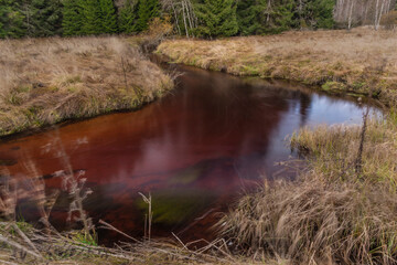 Jezerni creek in autumn color morning with red water and dry grass on meadow