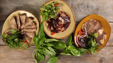 Oriental cuisine. Meat snack. Kazy. Homemade boiled horsemeat sausage with spices and fresh herbs. Beef tongue with onion and chili pepper. Rustic. Background image, copy space. Top view, flatlay