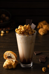 Tall glass cup with chocolate milkshake and caramel popcorn and chocolate muffin on wooden background