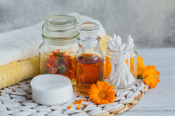 Natural cosmetic oil, tincture or infusion, cotton pad, sticks and towels with Calendula flowers on light background. Healthy skin care. Aromatherapy, spa and wellness concept