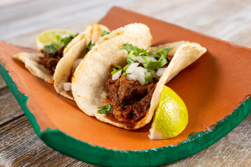 A view of street tacos on a clay shingle plate, in a restaurant or kitchen setting.