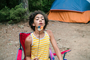 Teen girl blowing fire off of toasted marshmallows while sitting in campground by campfire