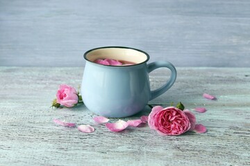 Hot tea with rose petals in a large cup, fresh flowers on a wooden table, healthy drink concept, home comfort 