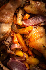 Baked chicken with vegetables in an iron brazier on a dark wooden background, chicken drumsticks with eggplant, pumpkin, onions and carrots baked in the oven