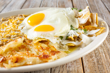 A closeup view of a Mexican breakfast plate, featuring chilaquiles, sunny side up eggs, in a restaurant or kitchen setting.